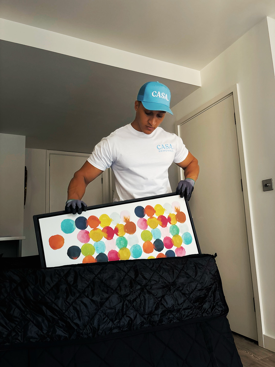 A CASA. crew member in branded cap and tee wrapping a framed print in a padded blanket